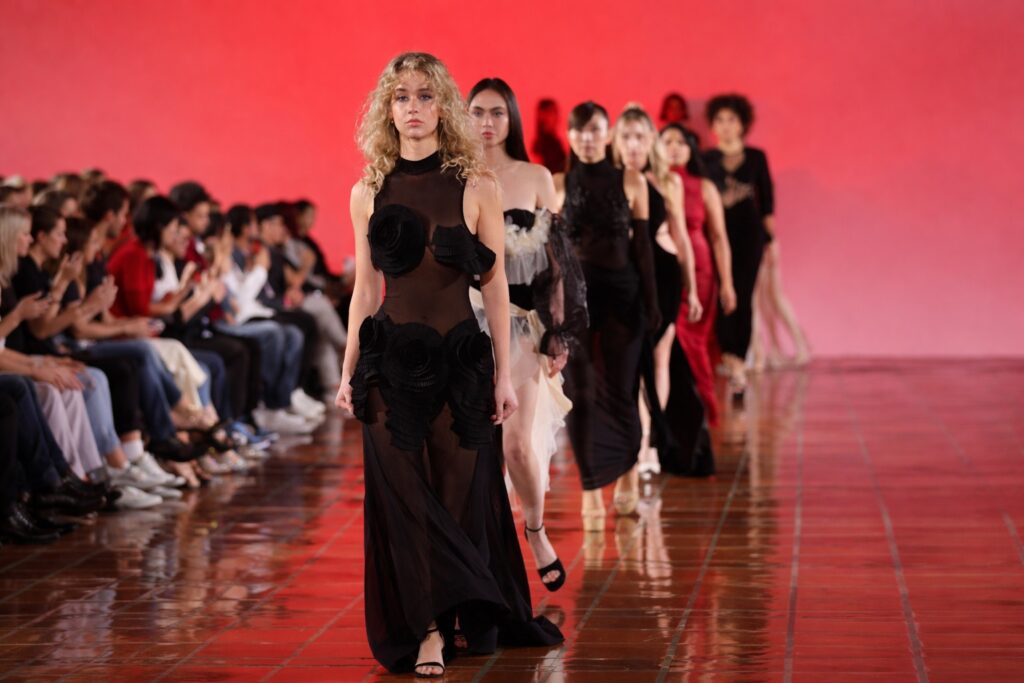 Runway finale at The Bureau at New York Fashion Week - models in black gowns against a red backdrop with the front row in view